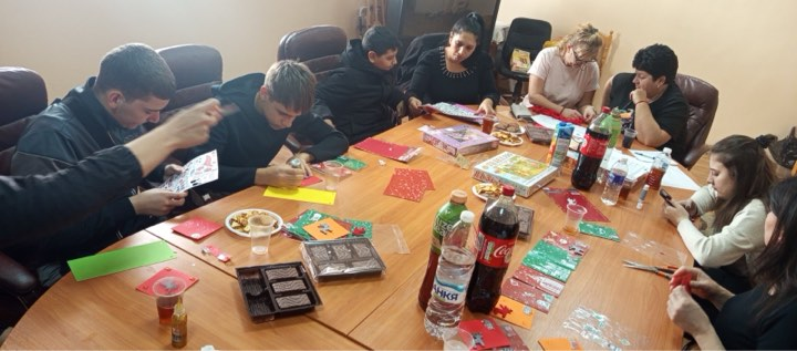 Mentors and mentees gathered around a table during a creative workshop, making handmade holiday cards and decorations using craft materials.