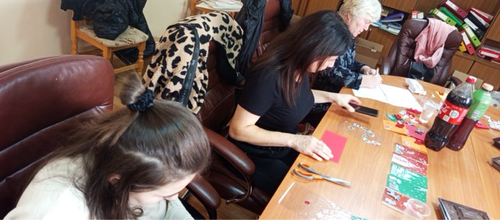 Mentors and mentees working together on arts and crafts activities at a table, creating handmade greeting cards in a collaborative workshop setting.